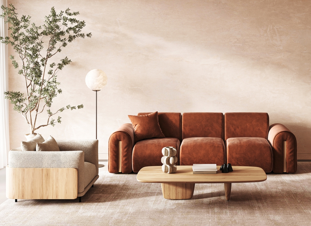 Japandi style living room featuring a rust-colored suede couch, light wood coffee table, beige chair, lamp, and tree